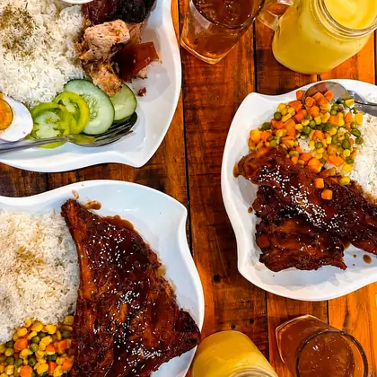 Several plates of belly, ribs and rice on the table with iced tea and mango shakes