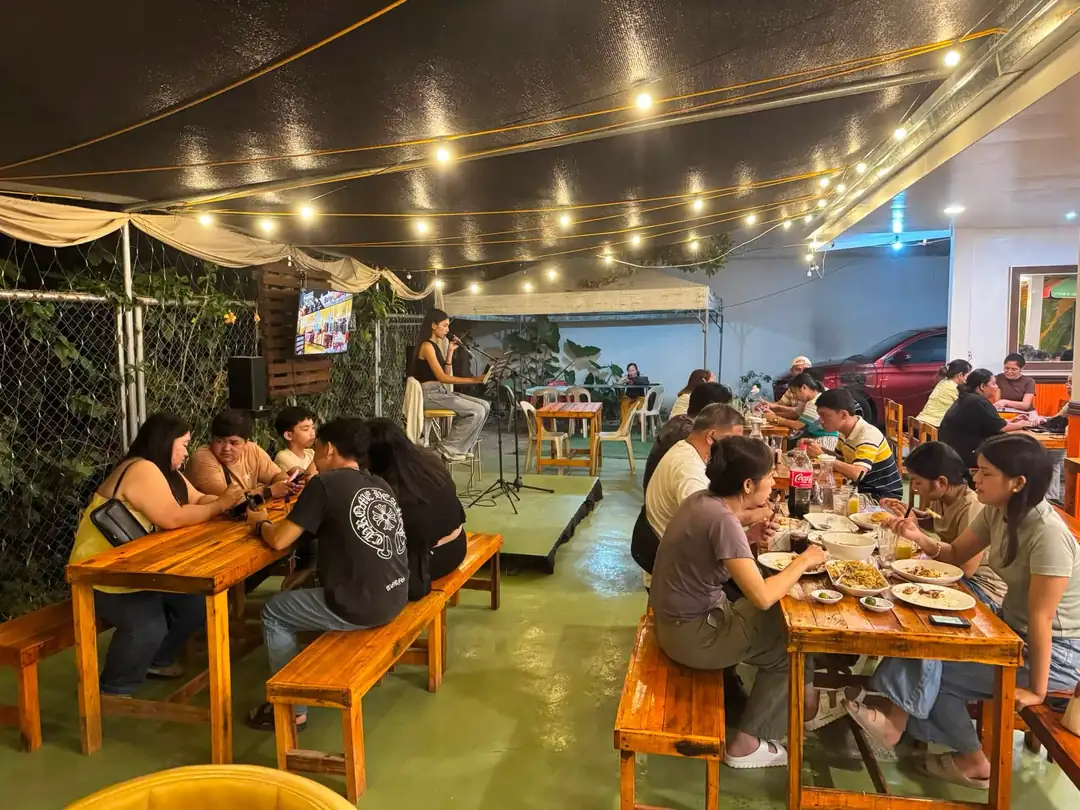 A singer performing under the string lights with diners at benches on both sides